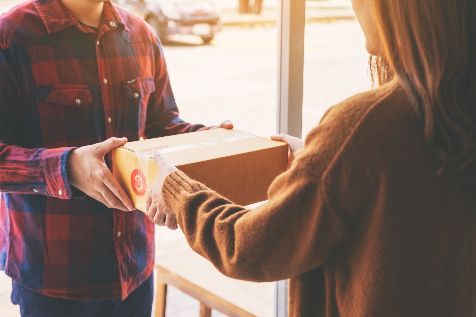 woman receiving parcel box from delivery man at the house's door; shipstation partner blog with Logicbroker